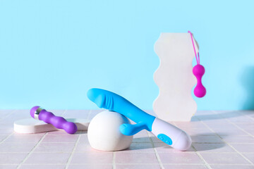Decorative stands with different sex toys on pink tile near blue wall