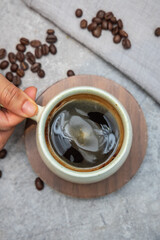 Shot from a bird eye view, a steaming cup of black coffee is held gently over a stone tabletop at a cafe.
