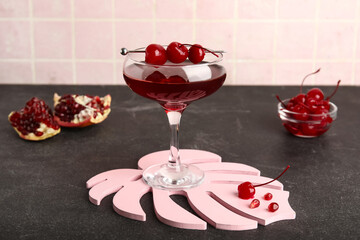 Glass of Cosmopolitan cocktail with cherries and pomegranate on black table