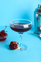 Glass of Cosmopolitan cocktail with pomegranate and cherries on blue background