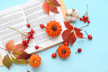 Beautiful composition with candles in shape of pumpkin, book and autumn leaves on blue background