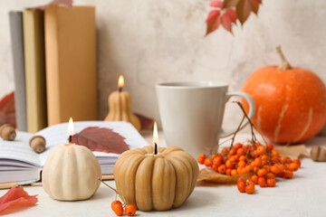 Beautiful autumn composition with burning candles in shape of pumpkin and book on table near beige...