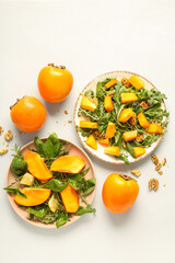 Plates of delicious salad with persimmon, walnut and lemon on white background