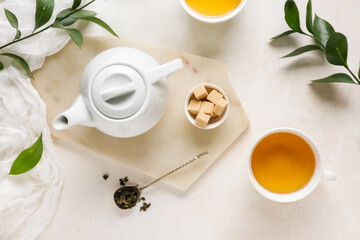 Cup of tea, teapot and spoon with dry leaves on light background