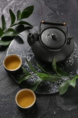 Teapot and cups of hot tea on black background