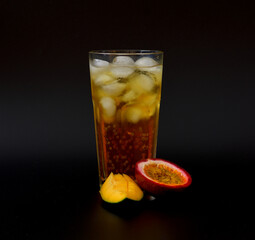 Mango and passion fruit juice in a tall glass with ice on a black background, pieces of ripe...