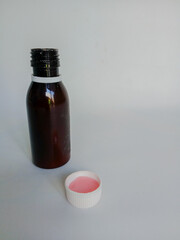 A dark medicine bottle with a white cap containing pink liquid placed beside it.