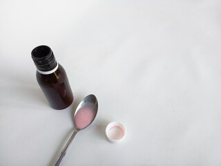 A dark medicine bottle with a white cap containing pink liquid placed beside it.