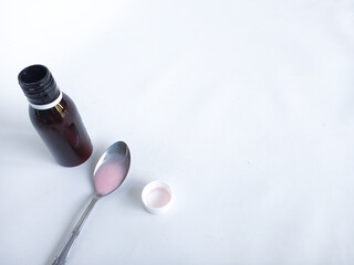 A dark medicine bottle with a white cap containing pink liquid placed beside it.