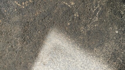 a close-up view of a rough, textured surface—likely an aged concrete or asphalt pavement. The...