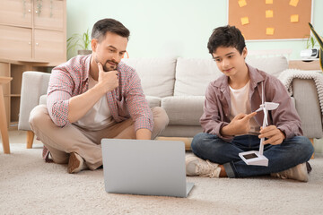Teenage boy with wind turbine model and his father using laptop at home