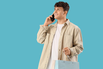 Handsome young man with shopping bags talking by mobile phone on blue background