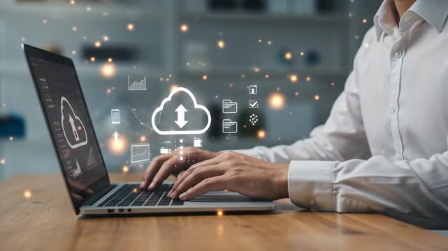 Person in white shirt uses a laptop displaying cloud computing visuals, with data icons and light particles, set on a wooden desk