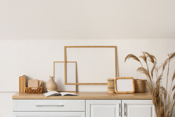 Stylish commode with different home decor and vase of dry reeds near white wall in room
