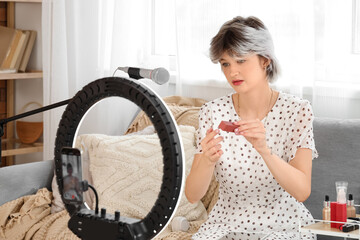 Female beauty blogger with lipstick recording video at home