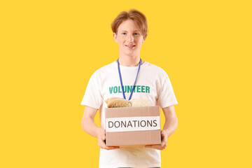 Young male volunteer with donations on yellow background