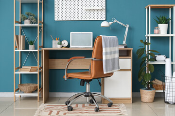 Stylish workplace with blank laptop, desk lamp and pegboard near blue wall. Freelance concept