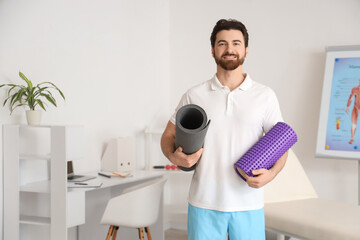 Male physiotherapist with foam roller and fitness mat in rehabilitation center