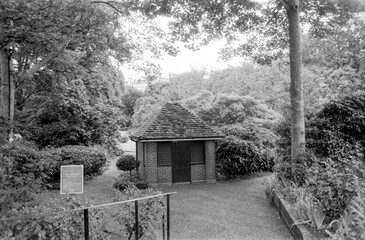 Vintage monochrome photo showing small brick building in lush garden