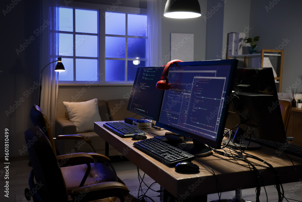 Poster programmer's desk with computer monitors and glowing lamps in dark office at night