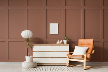 Brown leather armchair, pouf and chest of drawers near brown wall in interior of living room