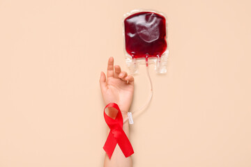 Female hand with red ribbon and pack for transfusion on beige background. Blood Cancer Awareness...