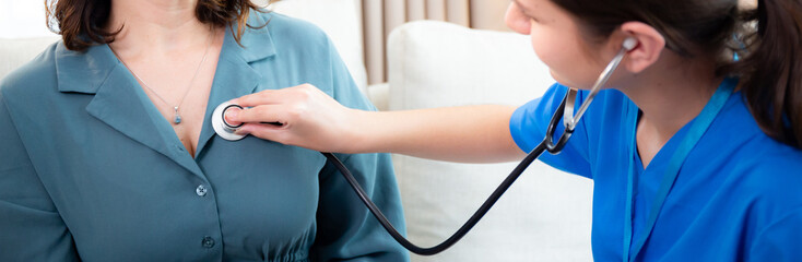 Caregiver young nurse woman examining woman with stethoscope for checkup sitting on sofa in living room at home, nurse checkup patient about cardiac, patient and insurance, medical and health.
