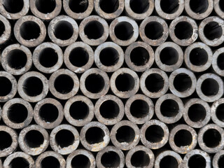 End view of stacked industrial metal tubes at building supply warehouse showing circular openings in repetitive geometric pattern. Construction materials creating abstract textured background.