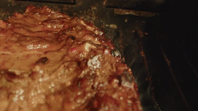 Beautiful macro dolly in of delicious spareribs being flame grilled on a dirty barbecue