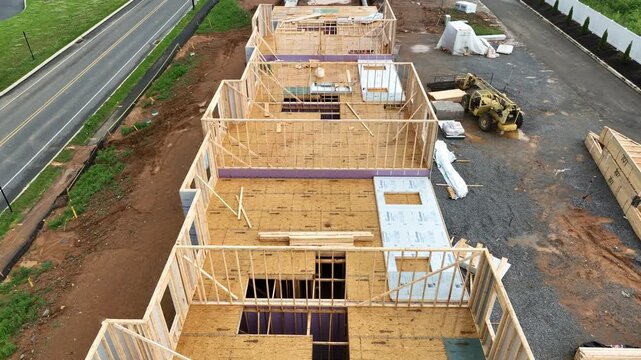 Wooden construction farming of row of houses during building phase. Cars on street. Sunny day in American suburb. Aerial Birds Eye shot.