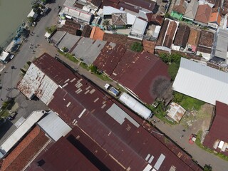 An aerial view of an industrial area with rusted rooftops, narrow streets, and surrounding houses.