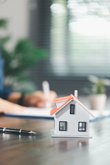Real estate agent and customer are discussing contract to buy house, with house model in background...