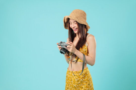 Happy young Asian woman with a camera is reviewing a photo on the screen, the girl is a tourist enjoying her travel and holding a camera during travel, headshots isolated studio blue background - Powered by Adobe