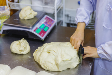 Bakery Worker Preparing Dough Using a Large Knife in a Bakery Kitchen with Industrial Equipment