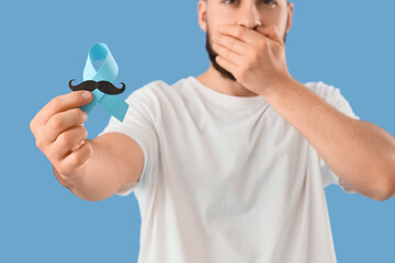 Young man with blue ribbon on color background. Prostate cancer awareness concept