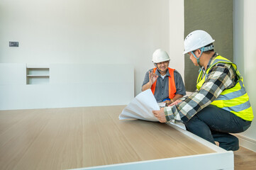Construction workers wea safety helmets and vests discussing while reviewing blueprints indoors du...