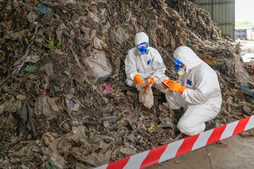 Two scientists wea protective suits and masks examining soil samples at a hazardous waste site for...