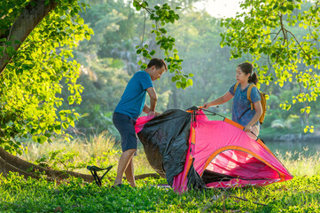 A man and a woman are setting up a tent in the woods.