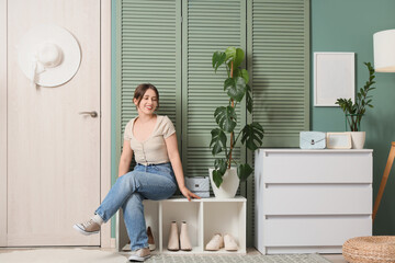 Young woman sitting on shoe stand in hallway