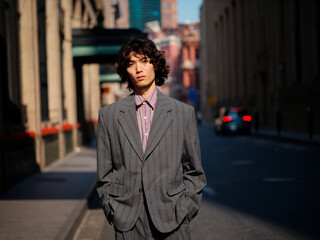 Portrait of handsome Chinese young man wearing gray suit posing in the street, young guy with black curly hair with urban background. Male fashion, cool Asian young man lifestyle.
