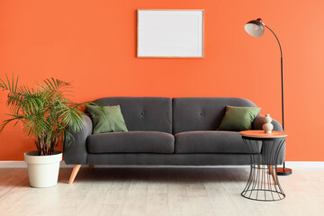 Comfortable sofa, table and floor lamp near orange wall in interior of living room