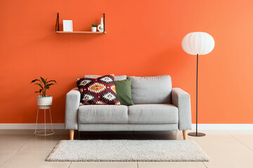 Comfortable grey sofa and floor lamp near orange wall in interior of living room