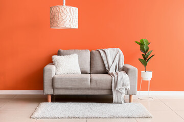 Comfortable beige sofa and houseplant near orange wall in interior of living room