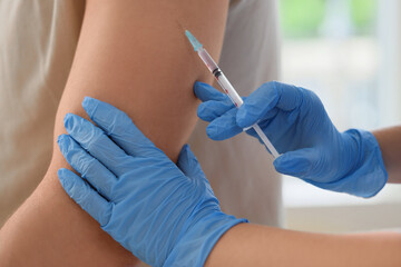 Young man receiving vaccine from doctor in clinic, closeup