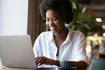 Smiling Black Woman Working on Laptop in Bright Cafe