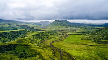 Obraz premium Vast green valley with rolling hills, winding river, and a distant mountain under a cloudy sky.
