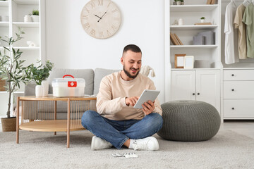 Young man with first aid kit using tablet computer at home