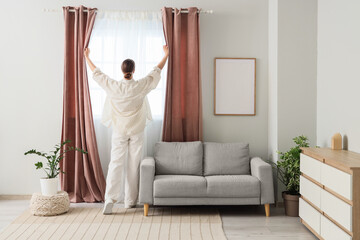Young woman opening pink curtains at home, back view