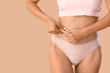 Young woman in underwear with cellulite problem on beige background