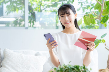リビングで通帳とスマホを見る若い女性
